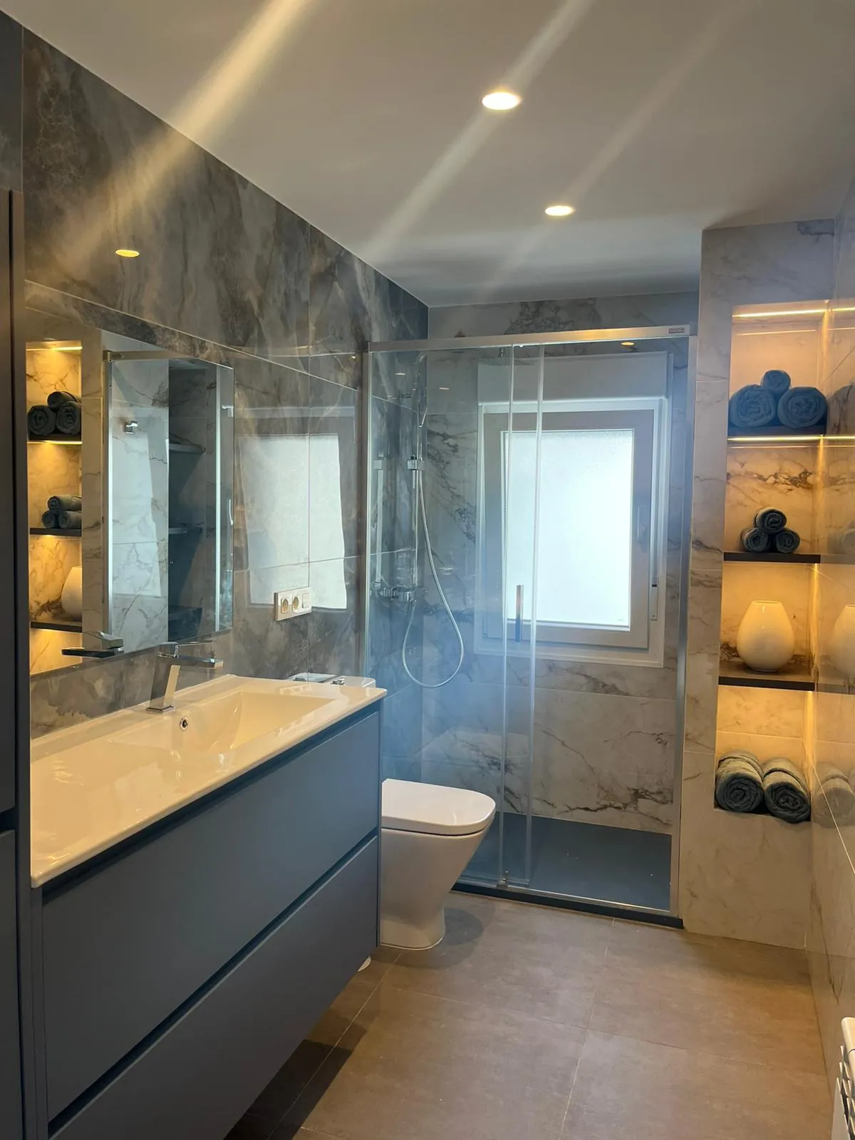 Baño con revestimiento gris veteado, ducha y mueble azul