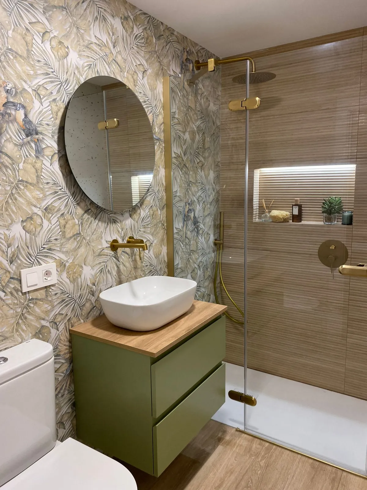 Baño con papel pintado tropical, mueble verde y grifería dorada